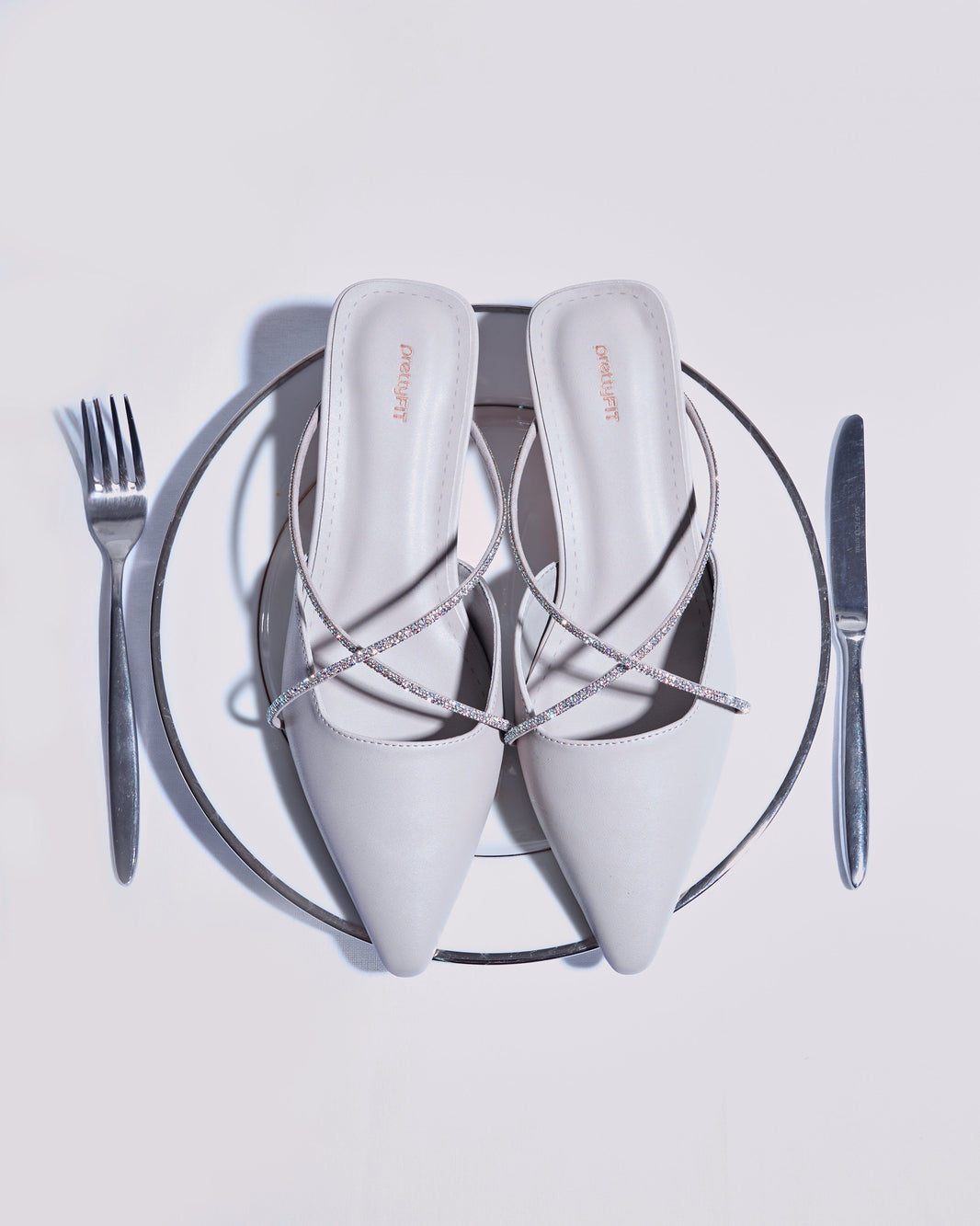 prettyFIT Jaime Heels on a dinner plate with cutlery—elegant straps meet artful styling in a fashion-meets-art concept.